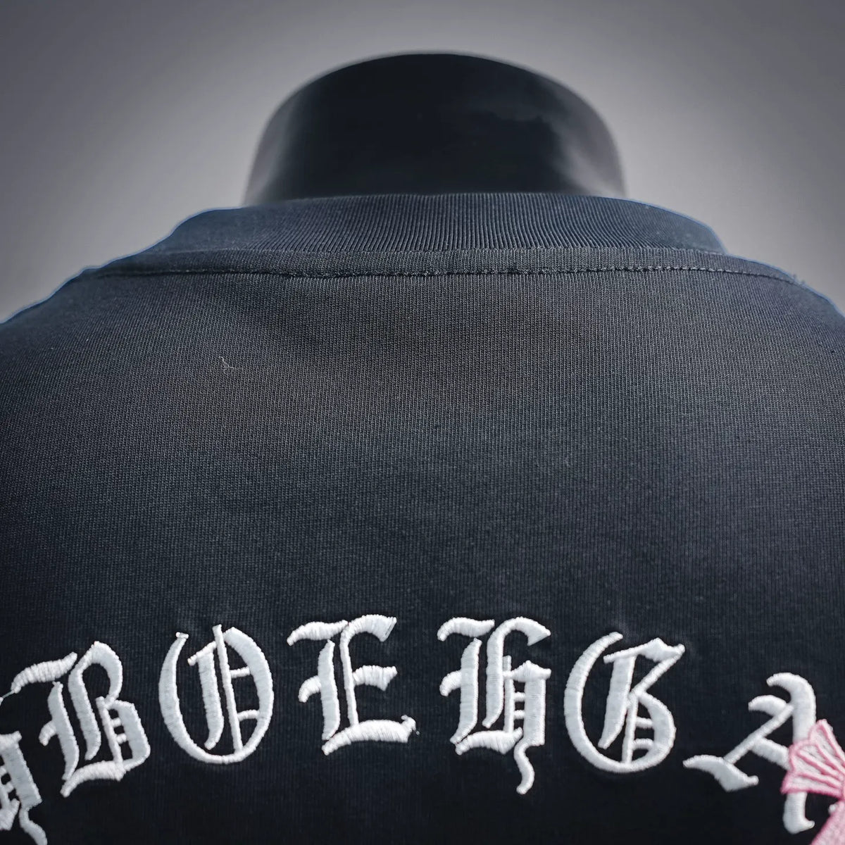 Dark T-shirt back collar with ribbed neckline and arched white graphic text.
