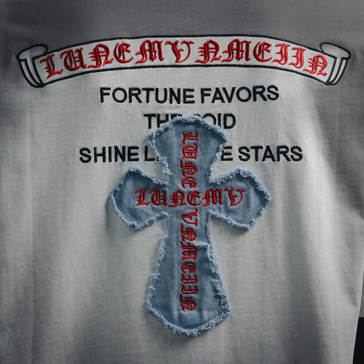 Close-up of denim-blue cross patch with red text embroidery on white T-shirt