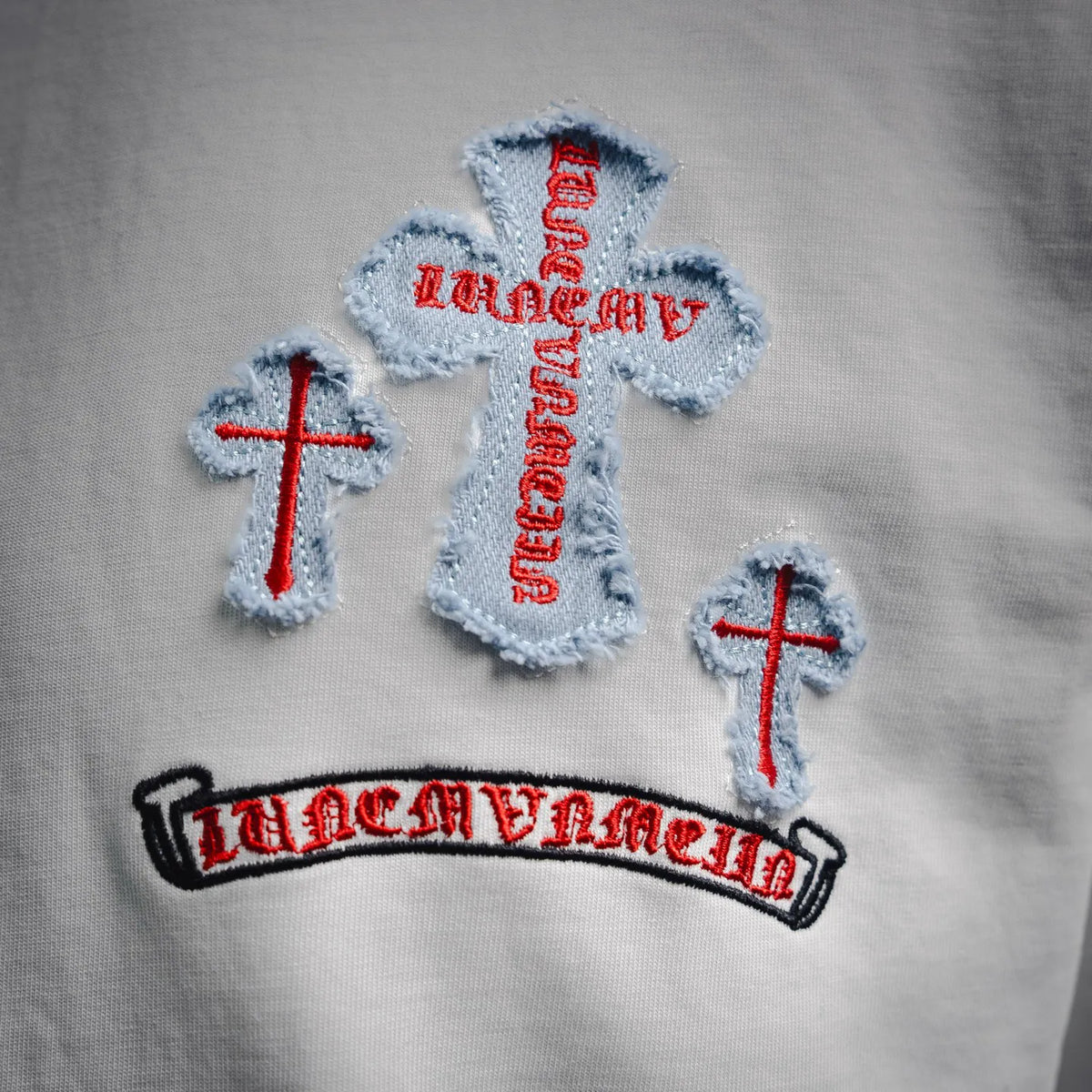 Close-up of embroidered cross patches and arched lettering on white T-shirt
