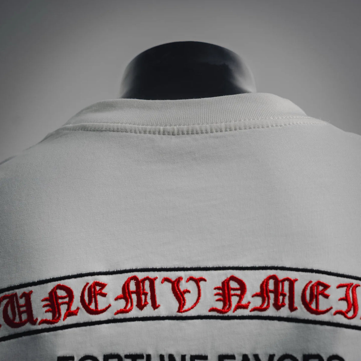White T-shirt collar and back hem detail with arched red/black lettering