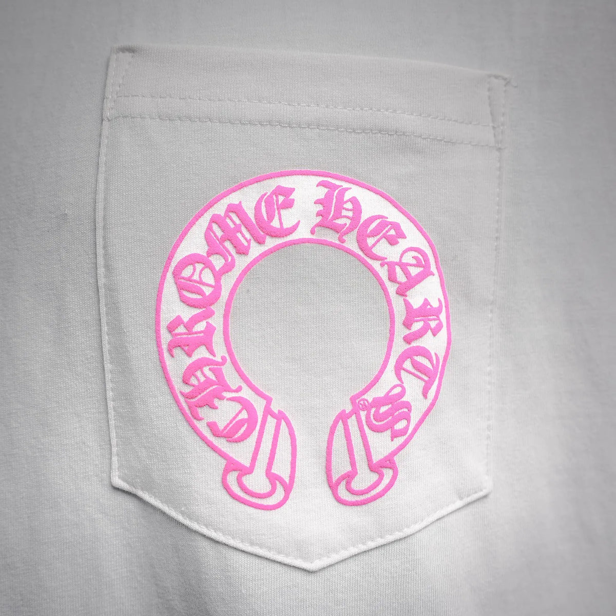 Close-up of pink circular logo on the front pocket area of a white T-shirt