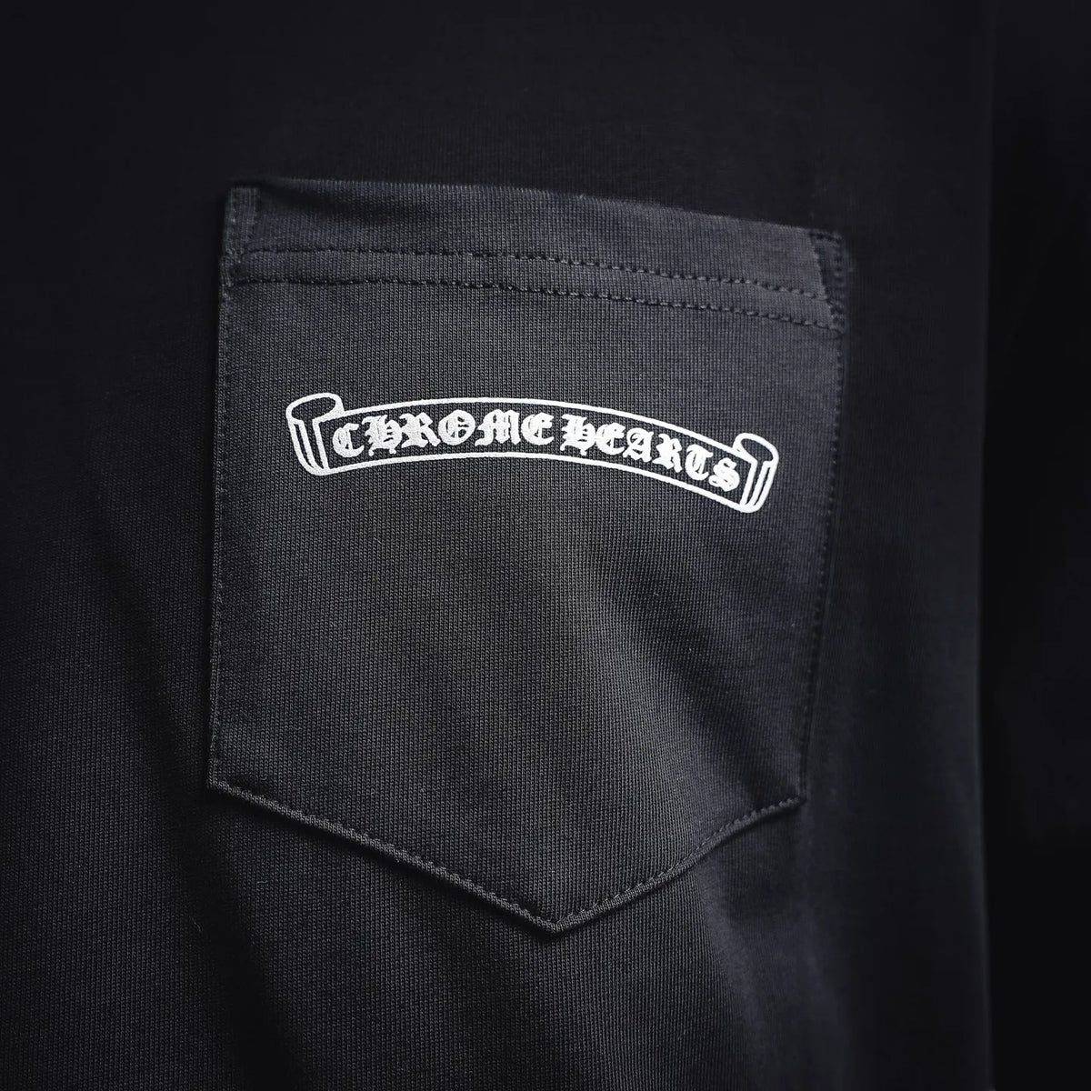 Dark T-shirt chest pocket with white Chrome Hearts-style logo patch