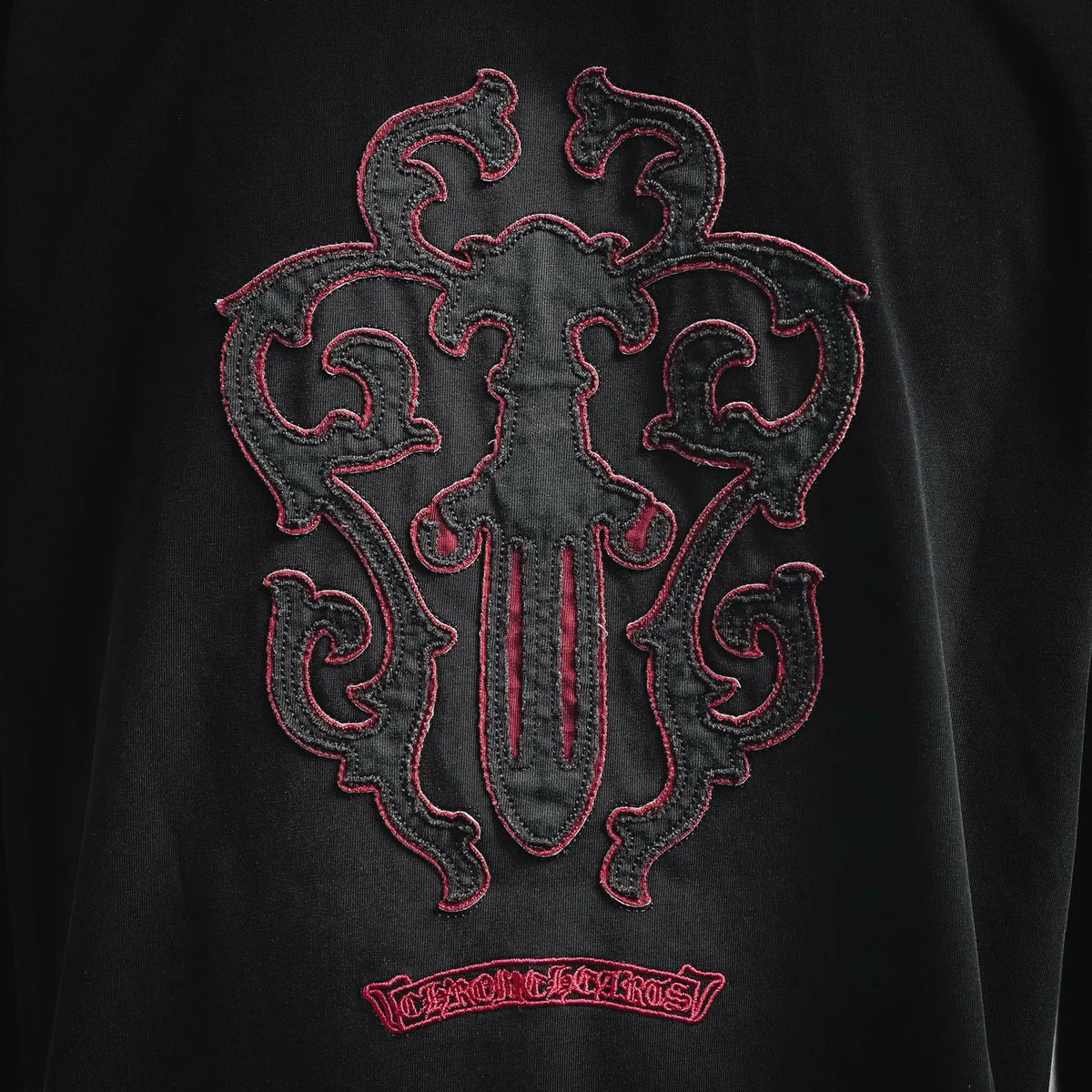 Black T-shirt back with large red-and-black ornamental crest embroidery and small text