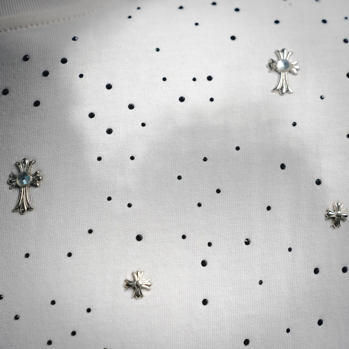 Close-up of white shirt fabric with rhinestone cross charms and black bead dot pattern
