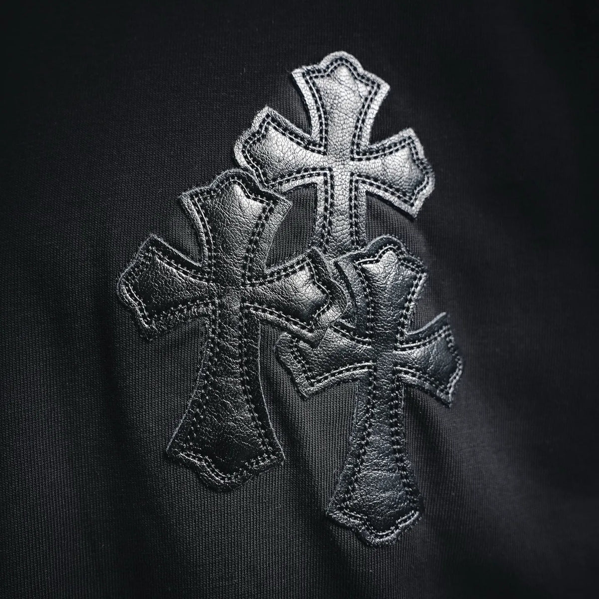 Close-up of stitched silver-tone cross applique on the front of a black T-shirt