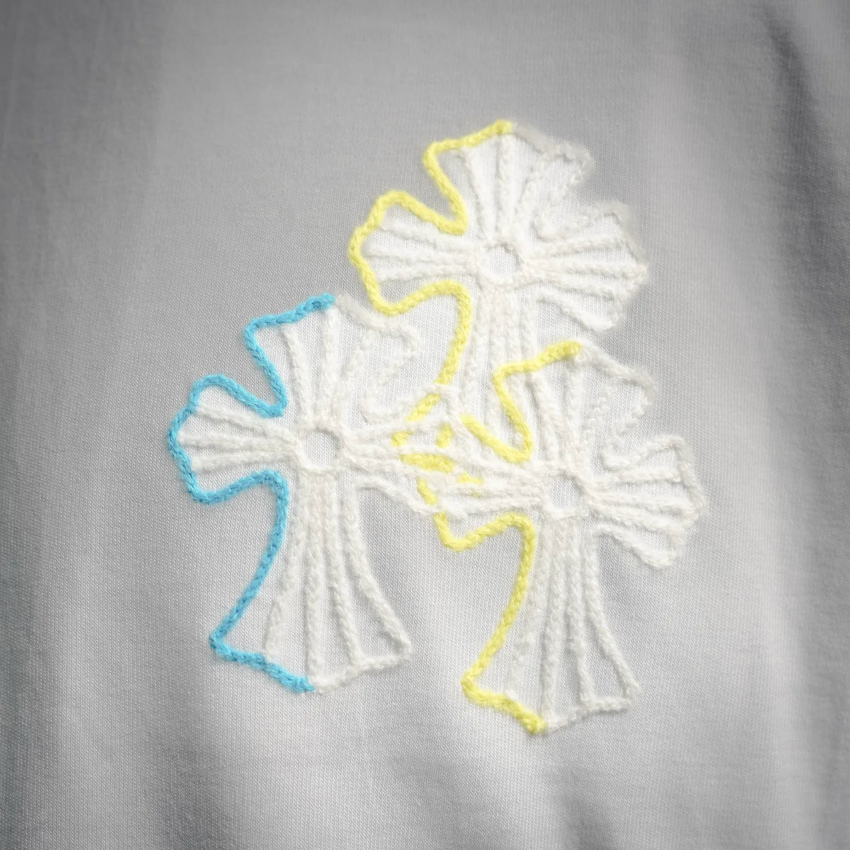 White T-shirt embroidery detail with yellow, blue, and white snowflake-style graphic