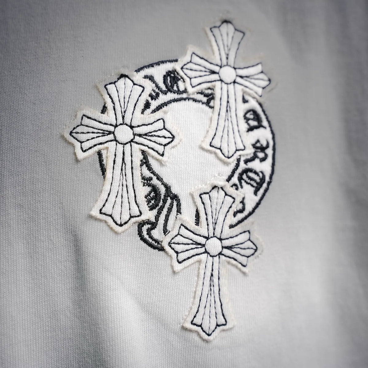Close-up: white T-shirt with embroidered circular cross graphic in black and gray
