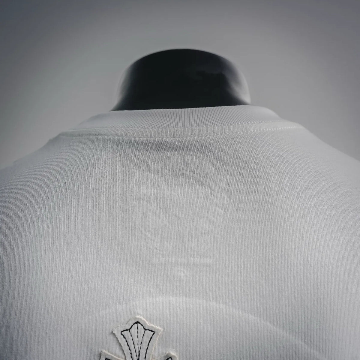 White T-shirt back yoke with subtle embossed logo and small cross detail at bottom