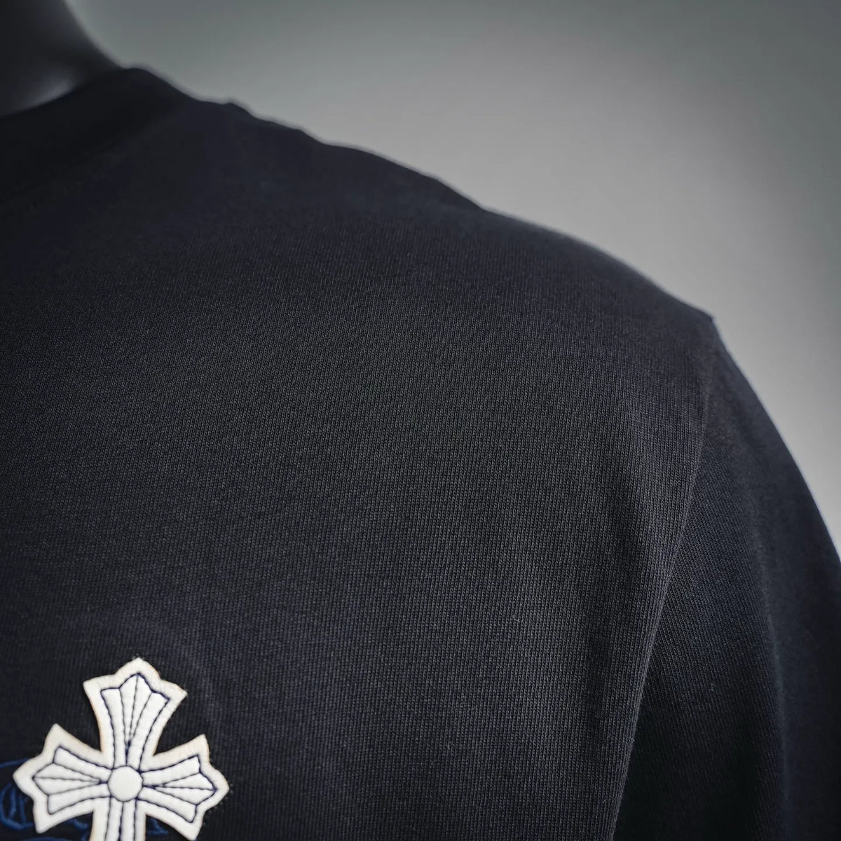 Black T-shirt shoulder close-up with small white cross patch