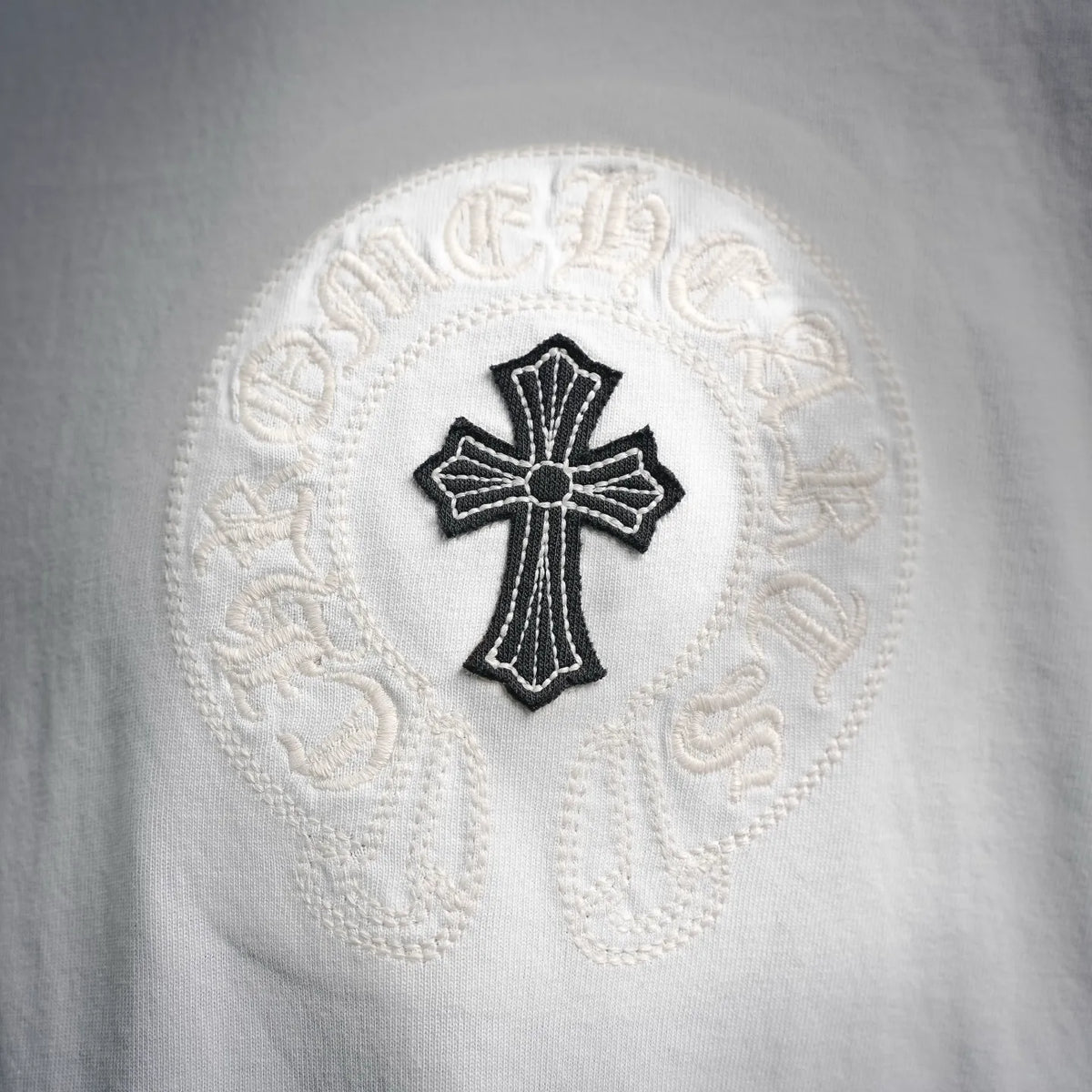 White T-shirt with close-up view of embroidered cross patch in a round emblem