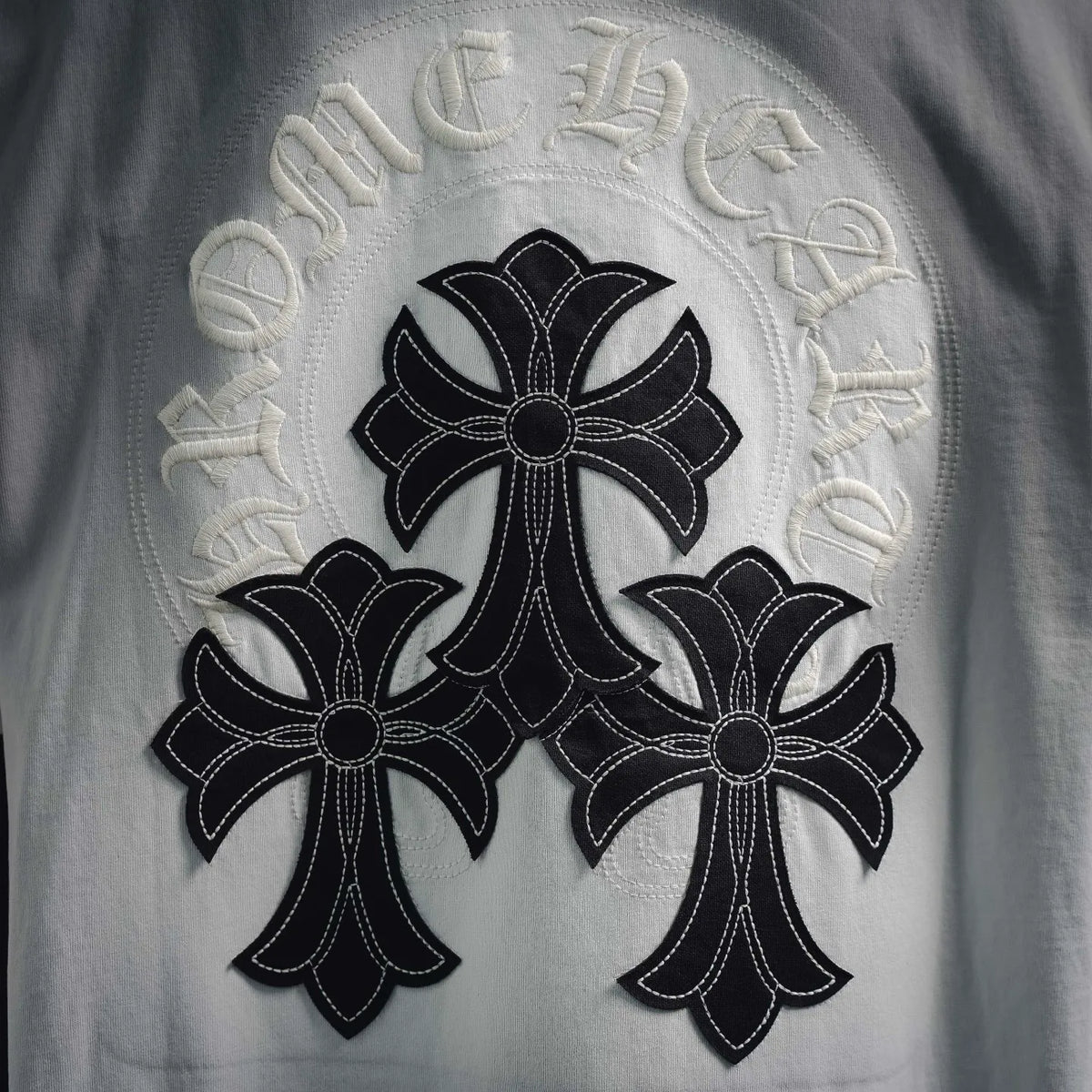 White T-shirt close-up of embroidered cross with three flower-like motifs