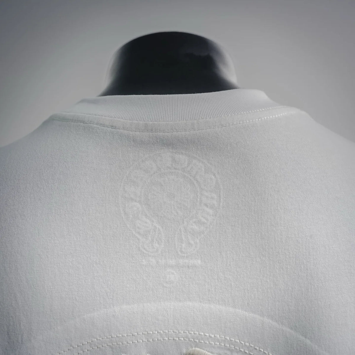 White T-shirt with crew neck collar and faint embroidered circular emblem near hem