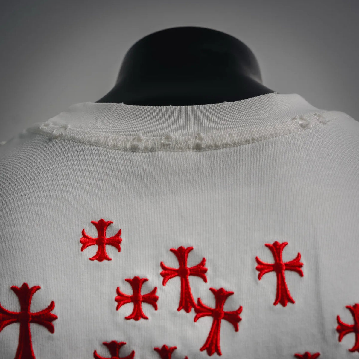 White T-shirt collar with small frayed edge; red cross embroidery below