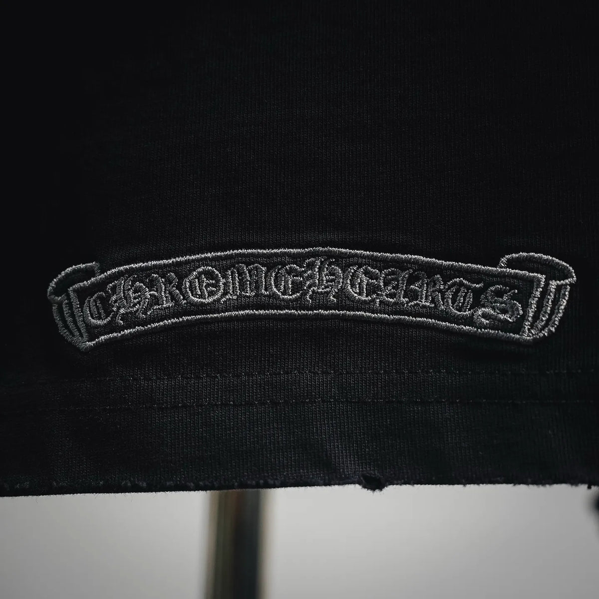 Black T-shirt hem with embroidered chrome-style logo patch
