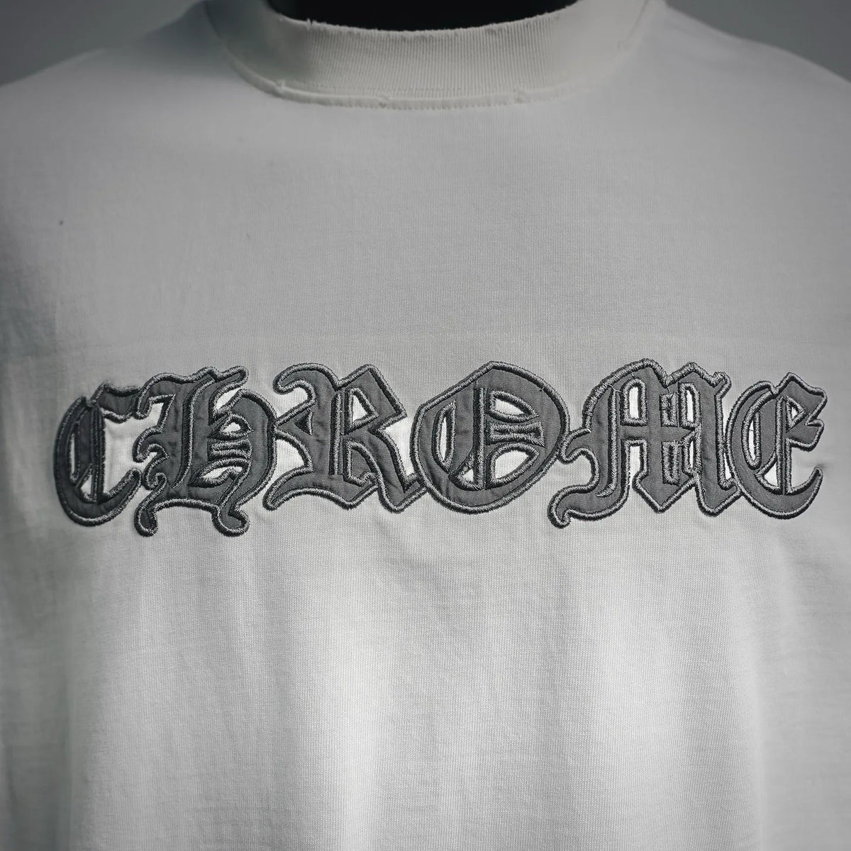 Close-up of front white T-shirt with dark embroidered-style text logo
