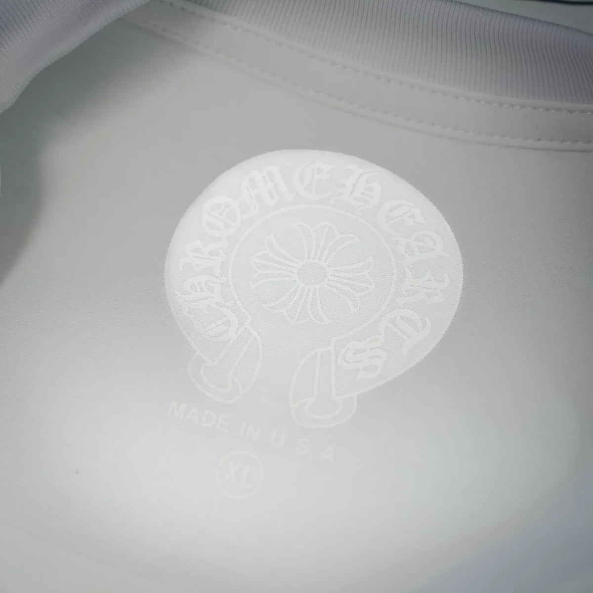 Close-up of raised emblem graphic on white T-shirt back; includes small text