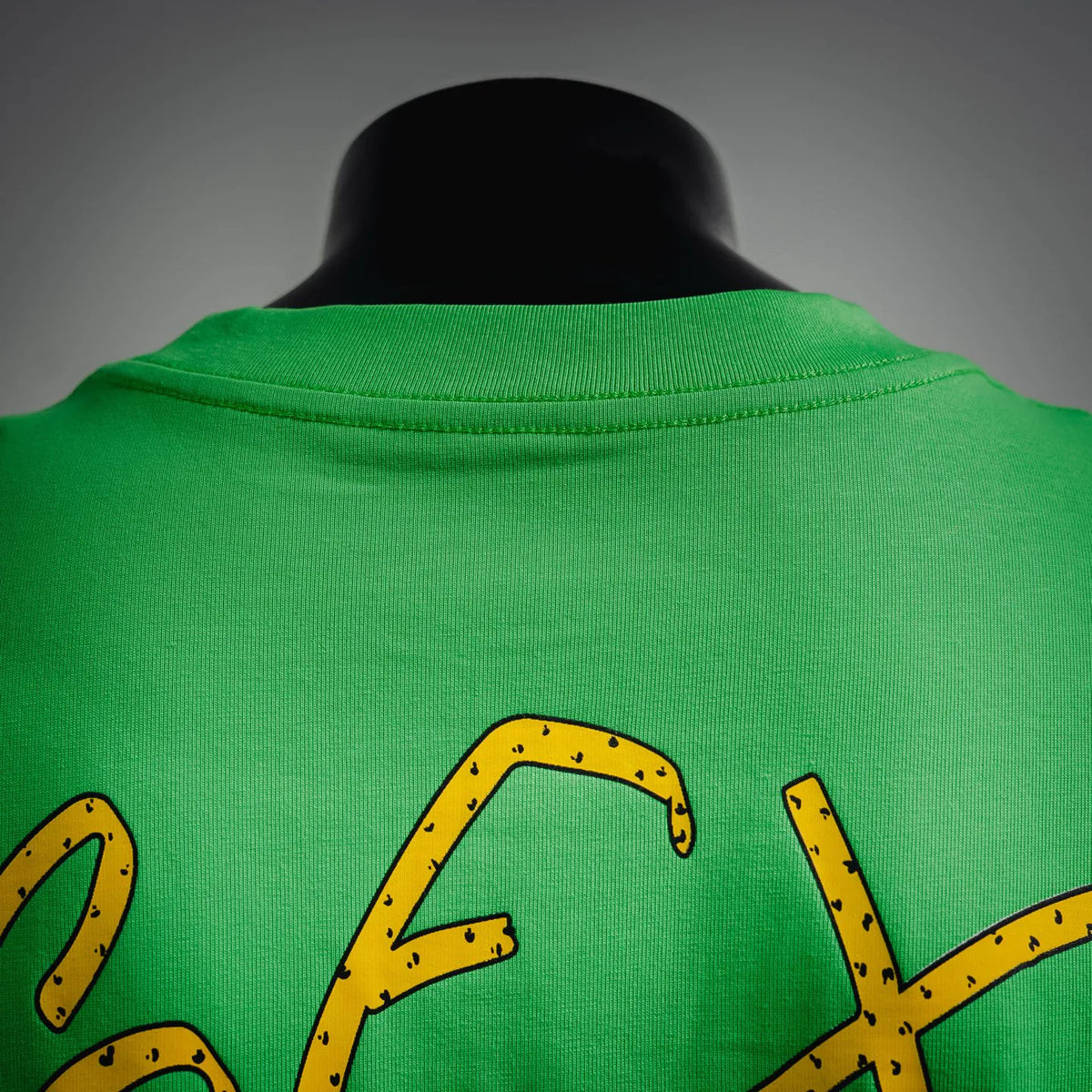 Green T-shirt back with large yellow letter graphic near shoulders