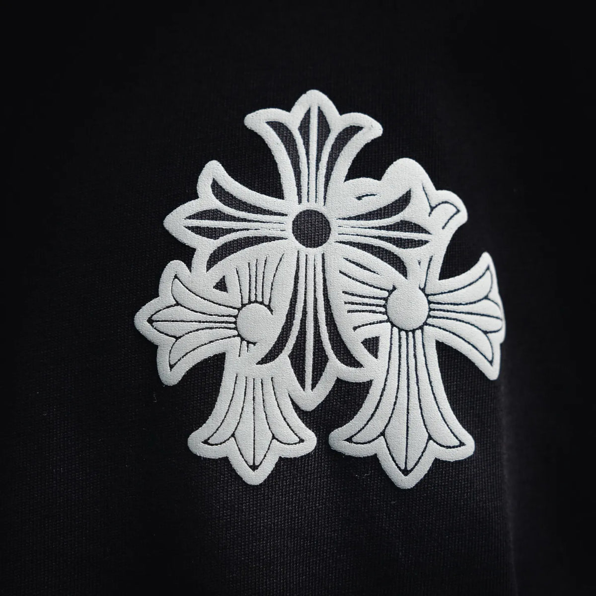 Close-up of white floral cross logo on the chest of a black crewneck T-shirt