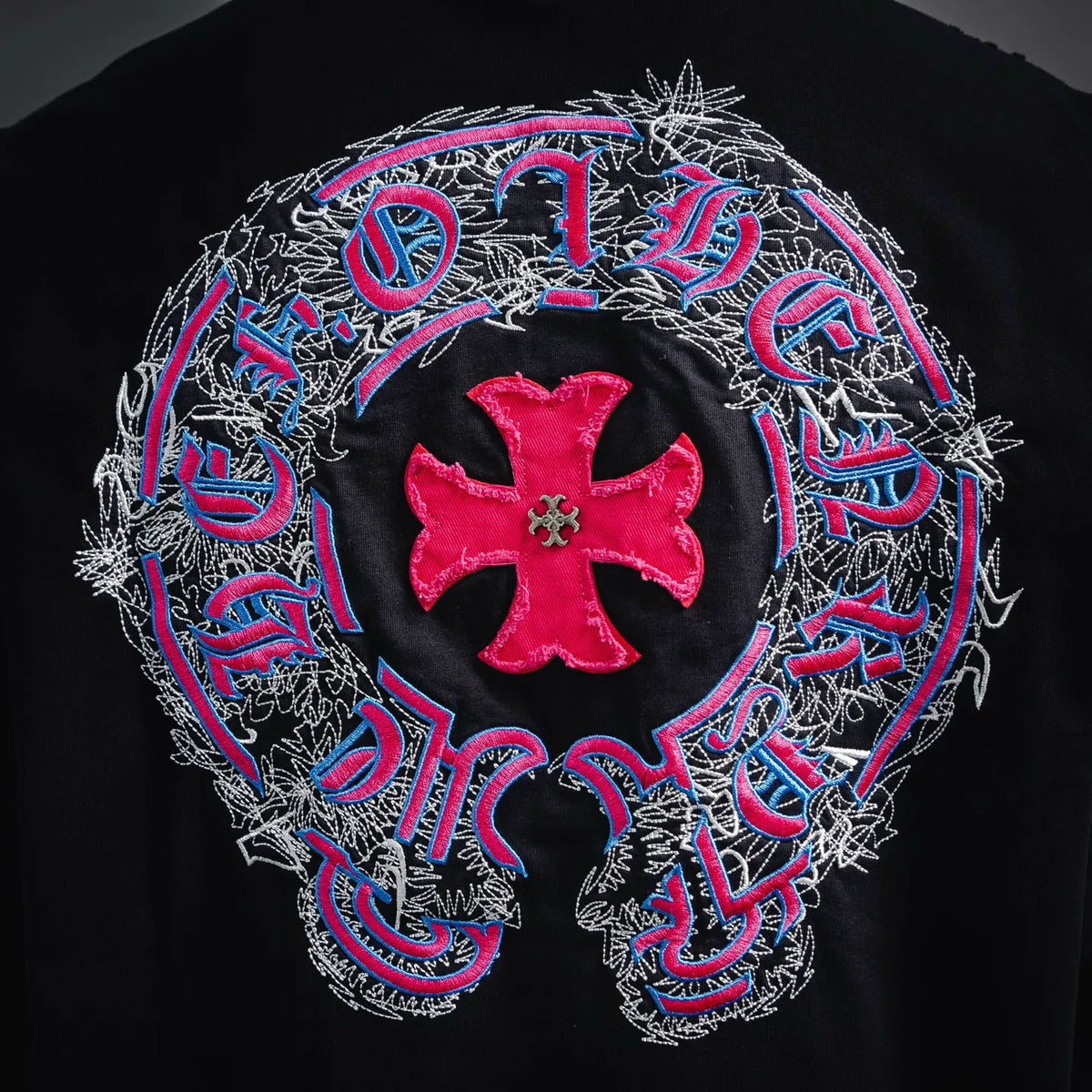 Close-up of black T-shirt back: red cross emblem with blue-pink ornate embroidery