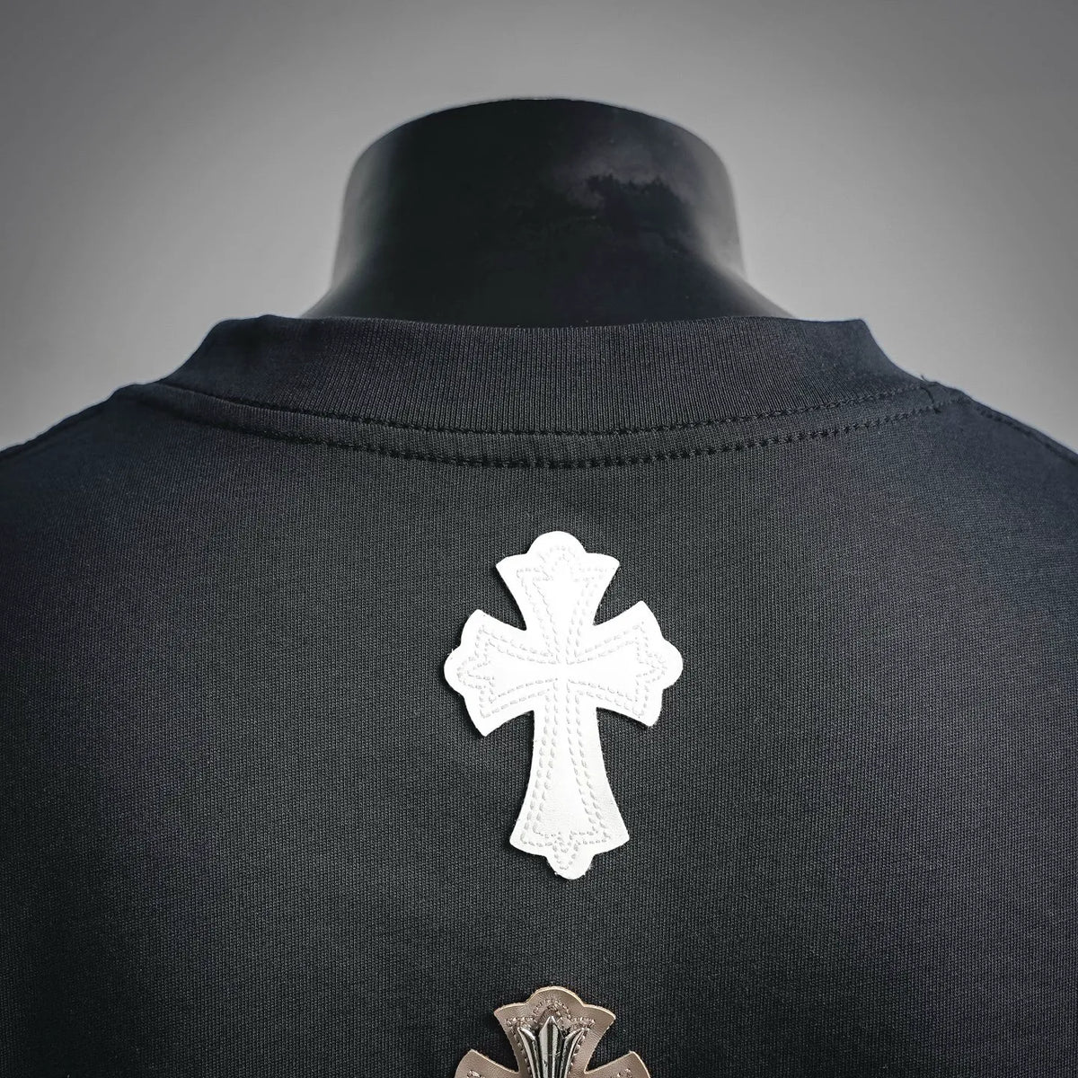 Dark T-shirt collar area with single white embroidered cross patch