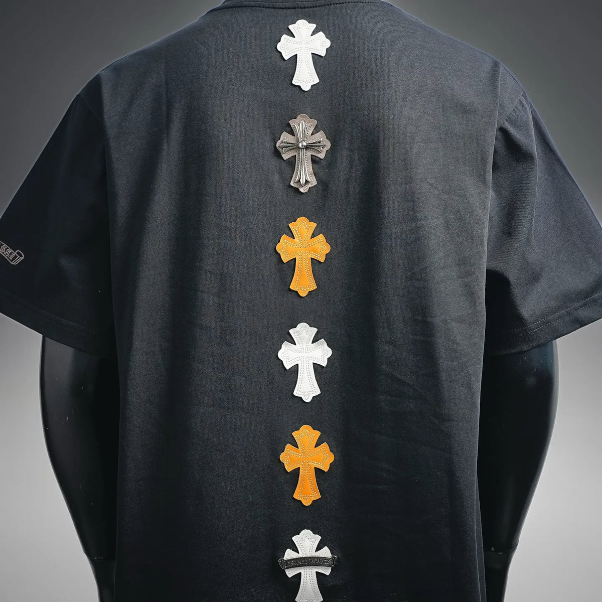 Dark short-sleeve T-shirt back with column of cross patches in white, gray, and gold