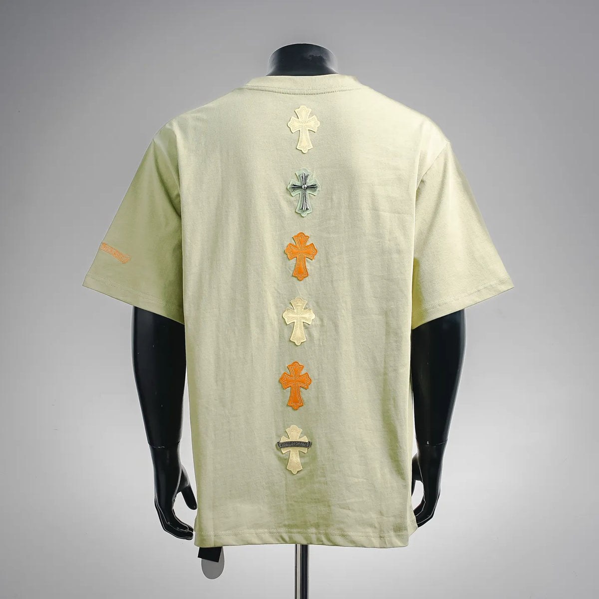 Light green short-sleeve T-shirt with vertical row of multicolor cross patches on back