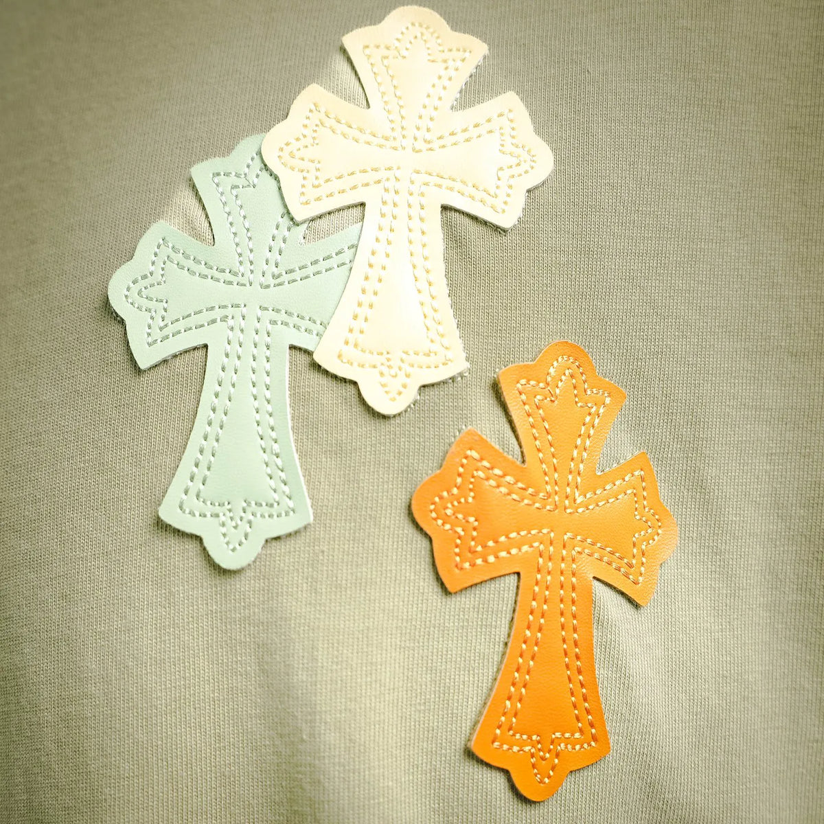 Embroidered cross patches in white, teal, and orange on light green fabric