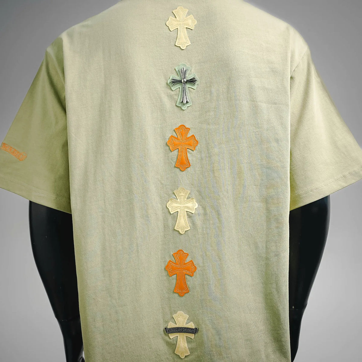 Light green short-sleeve T-shirt with stacked multicolor cross patches on back