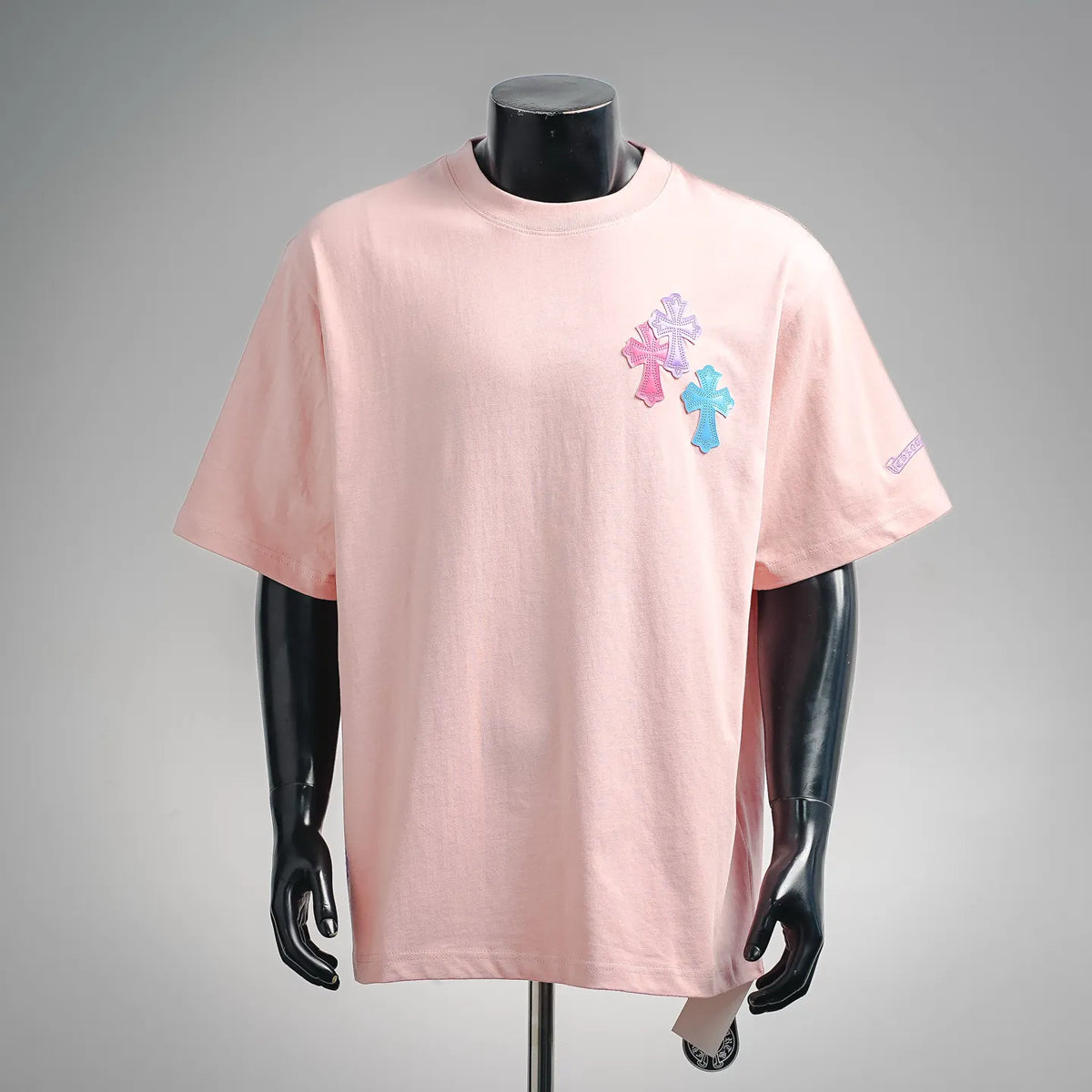 Pink short-sleeve T-shirt with multicolor cross patch graphic on chest.