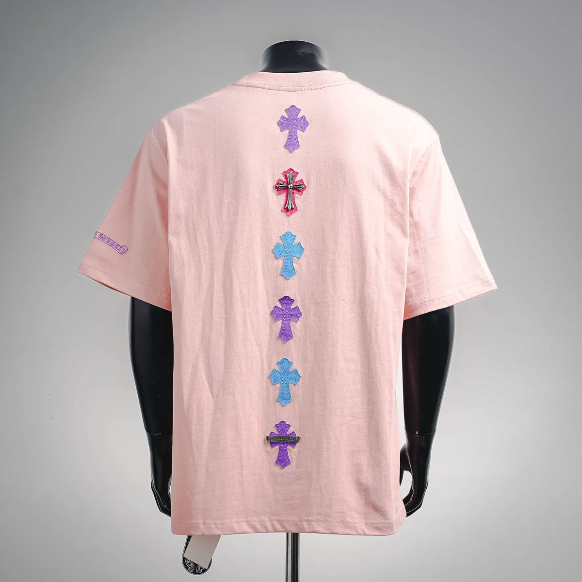 Pink T-shirt with vertical row of embroidered cross patches on the back.