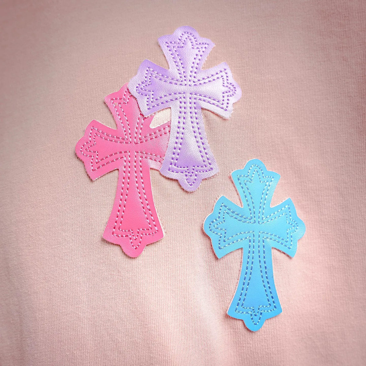 Close-up of multicolor cross appliques on pink short-sleeve T-shirt.