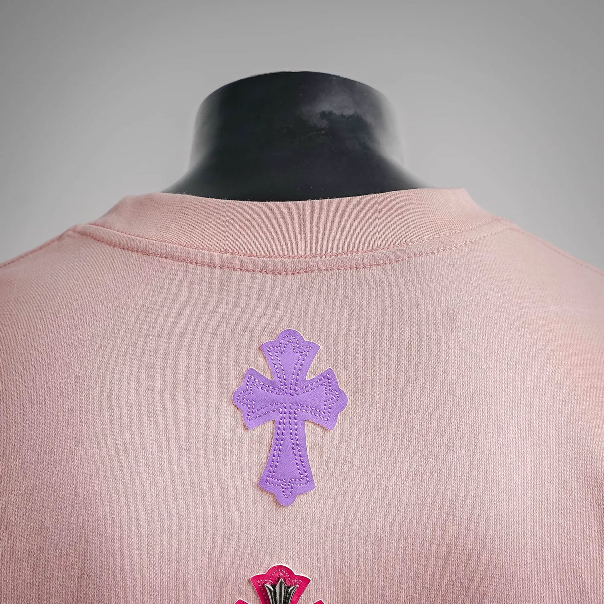 Pink T-shirt back neckline with small purple and red cross patch embroidery.