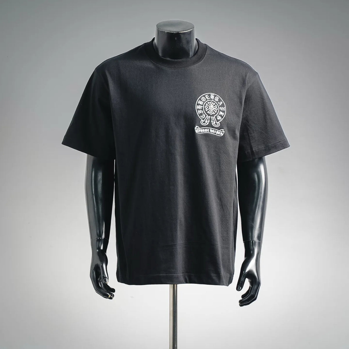 Black short-sleeve graphic T-shirt with white round chest emblem and text below.