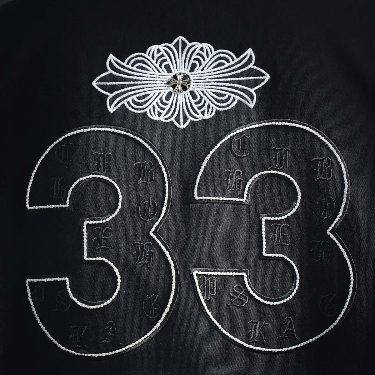 Close-up of white embroidered “33” and decorative flower emblem on black shirt.