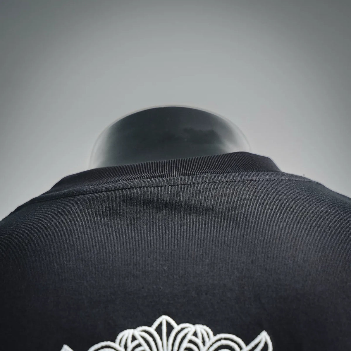 Black T-shirt back neckline and shoulder seam with white embroidered emblem.