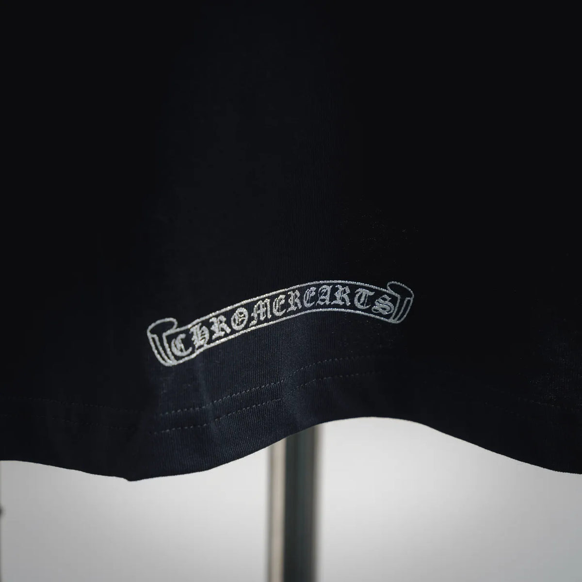 Black T-shirt hem with arched embroidered wordmark patch in white thread