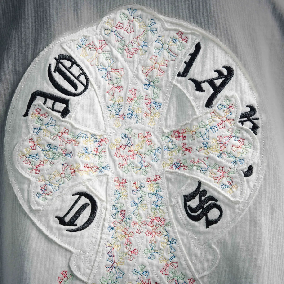 Close-up: White T-shirt circular embroidery with colorful cross shapes and letter icons