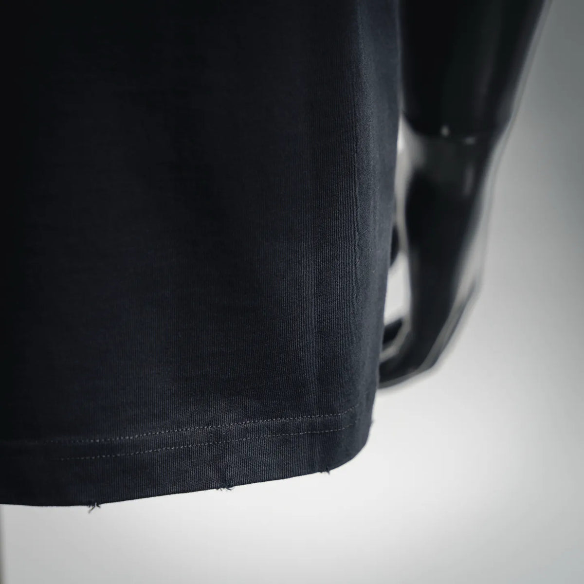 Close-up of black T-shirt fabric with stitched hem and side drape.