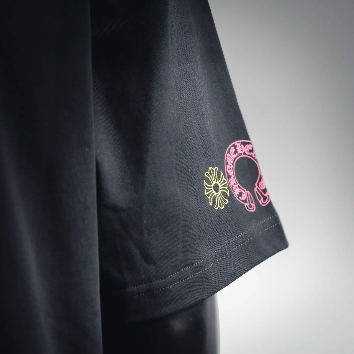 Black T-shirt sleeve cuff with small pink and white embroidered logo