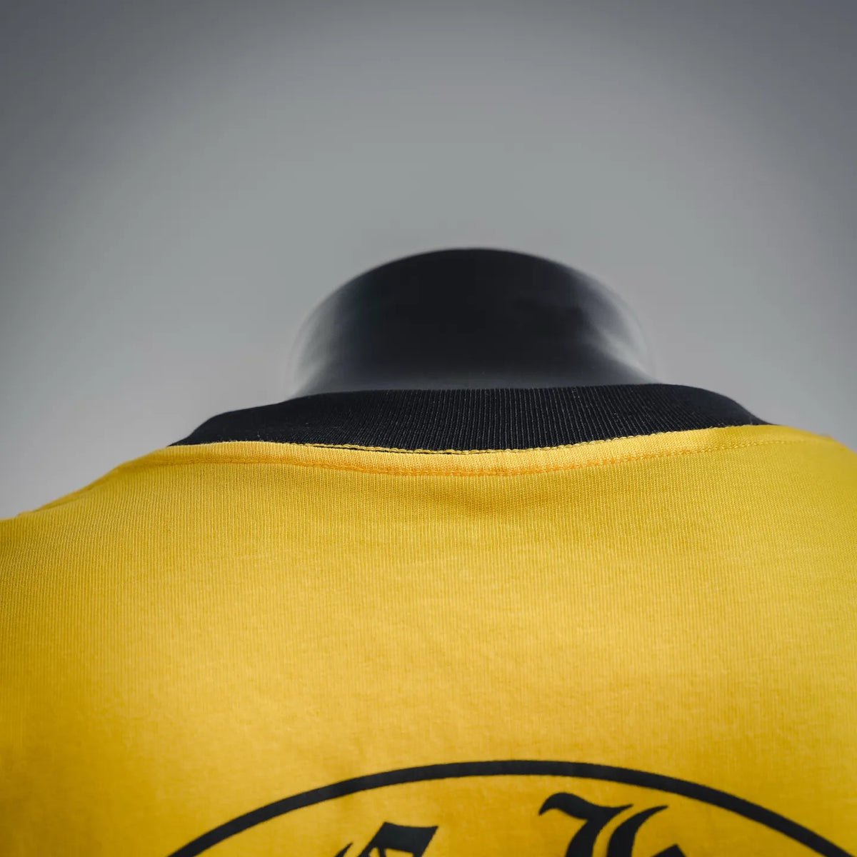 Yellow T-shirt neckline with black collar band, back graphic partially visible