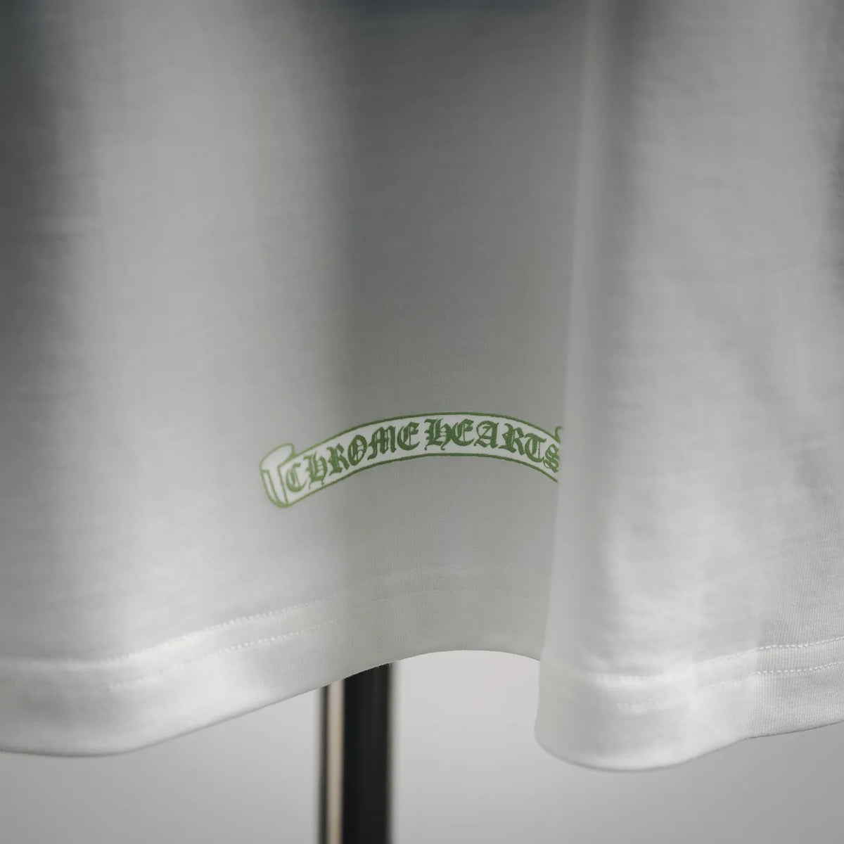 White T-shirt sleeve hem with green Chrome Hearts logo patch