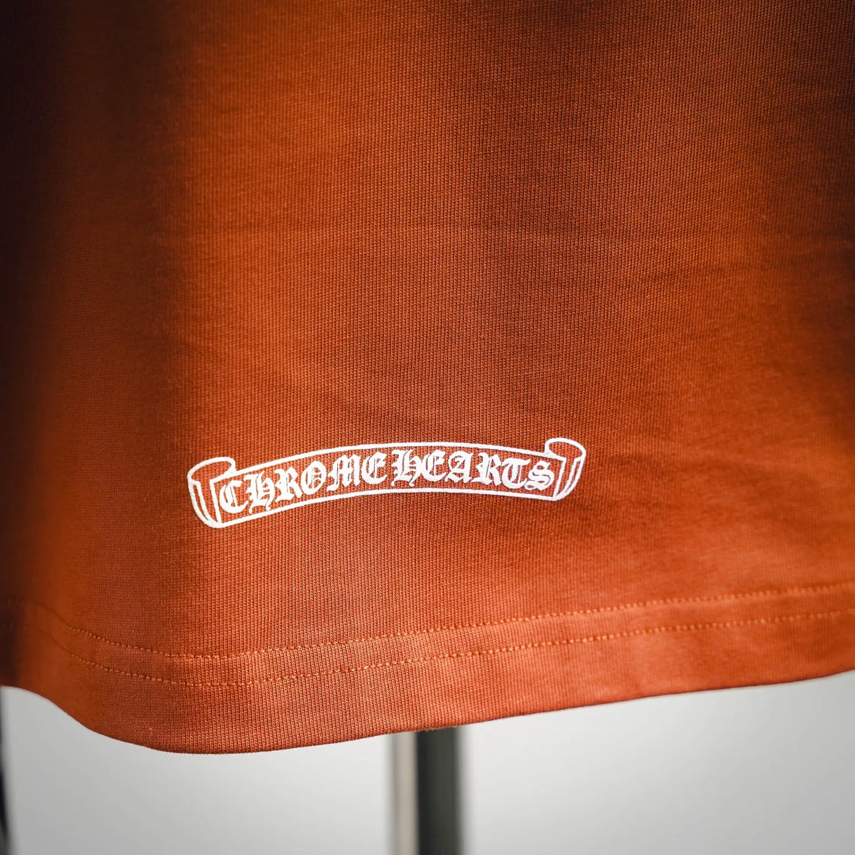Orange T-shirt hem with white brand text print near bottom edge