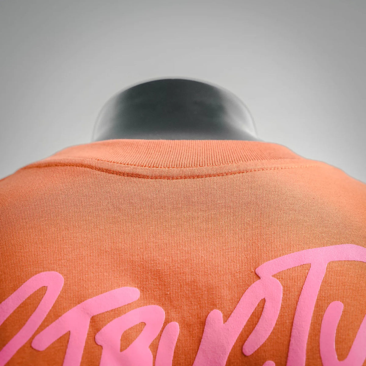 Orange T-shirt back with partial pink lettering across upper back