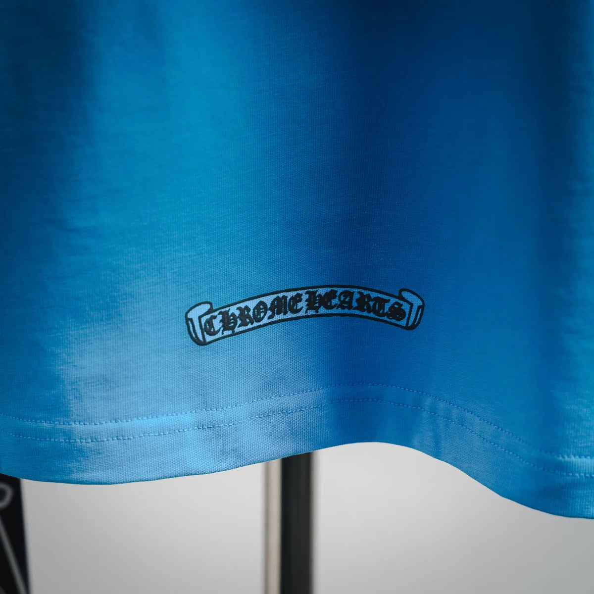 Light blue T-shirt hem with embroidered-style Chrome Hearts logo patch
