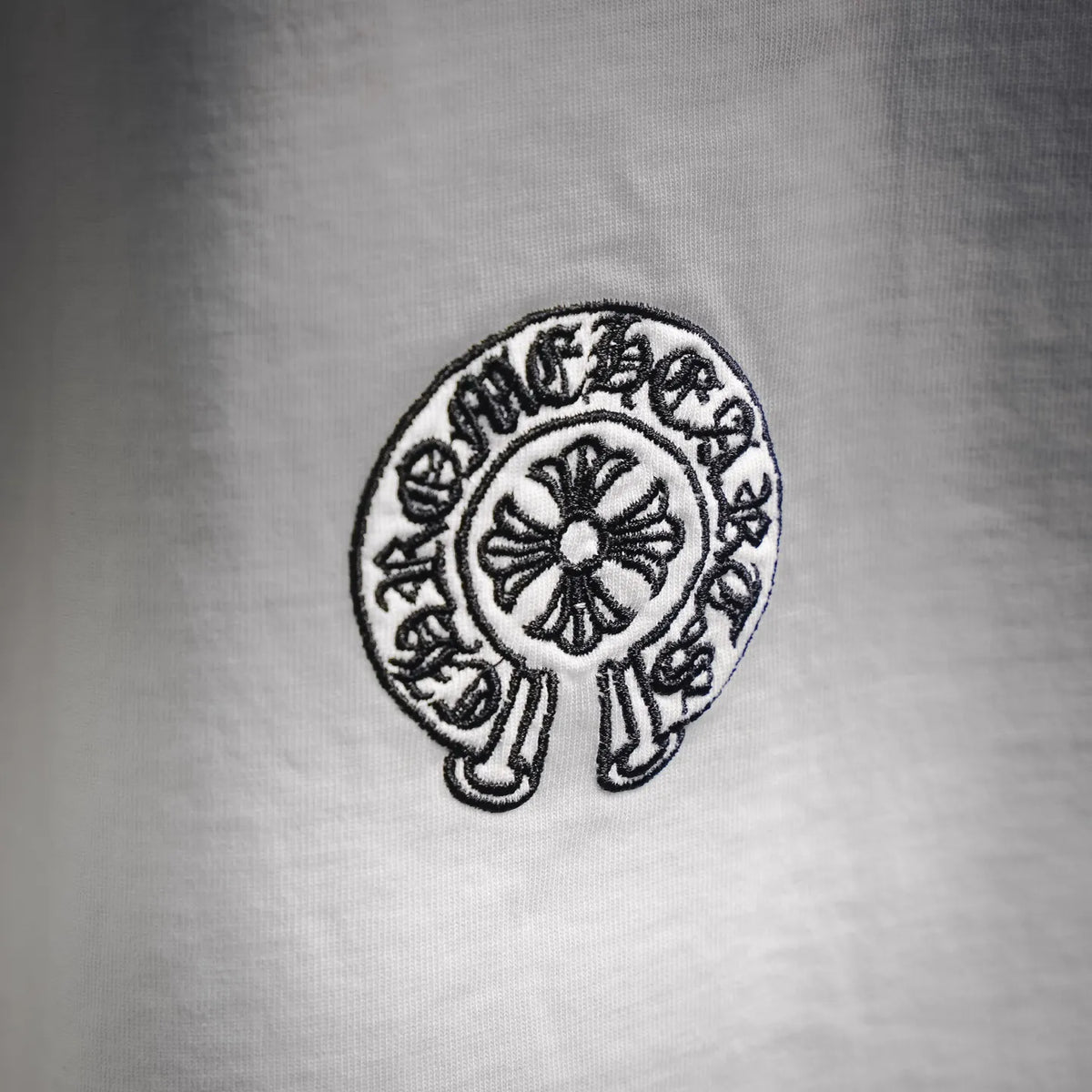 Close-up of white T-shirt chest patch: circular black-and-white emblem with flower