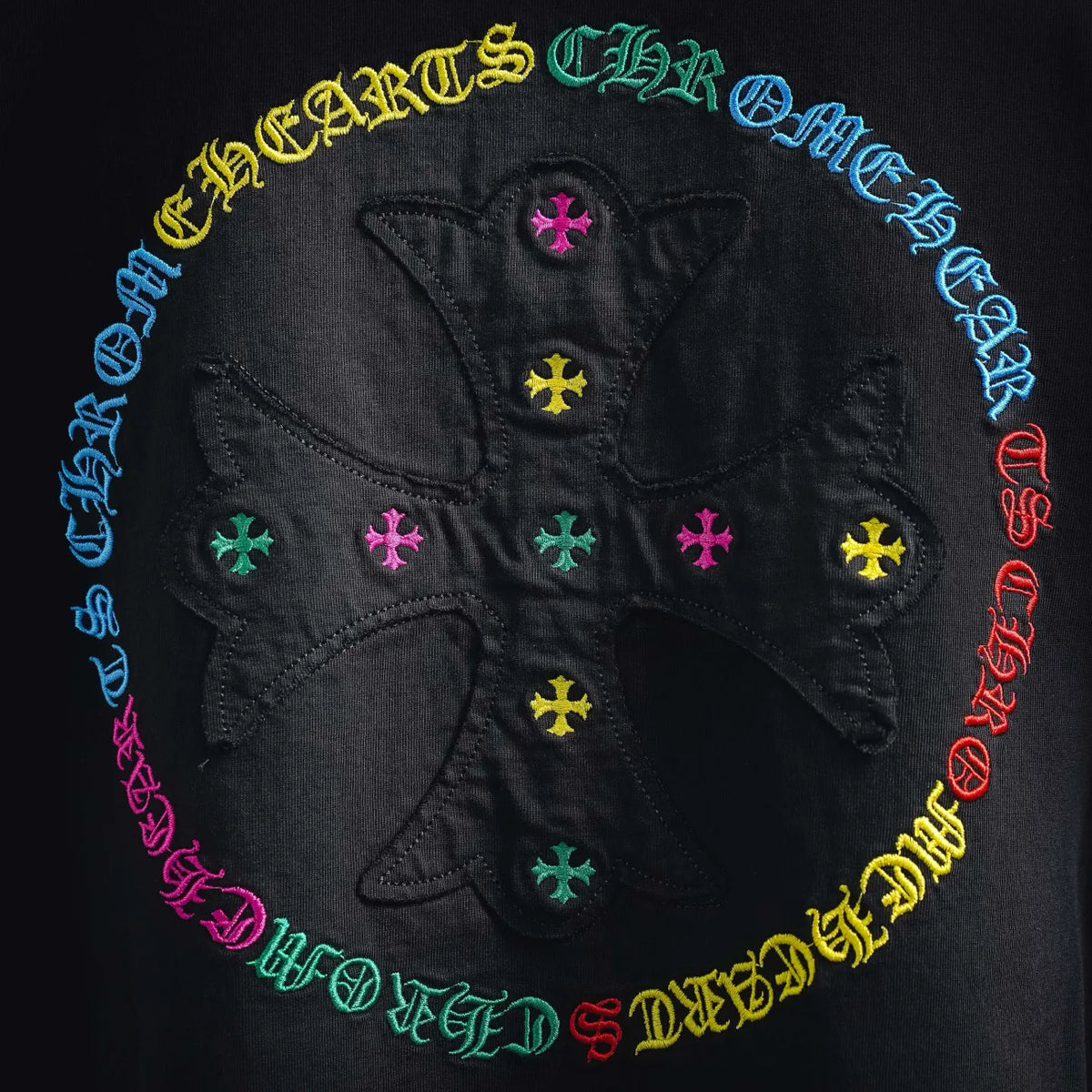 Close-up of back circular multicolor logo with cross symbols on black T-shirt.