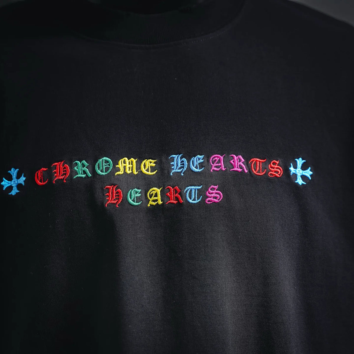 Black T-shirt chest graphic with multicolor gothic-style lettering and star accents.