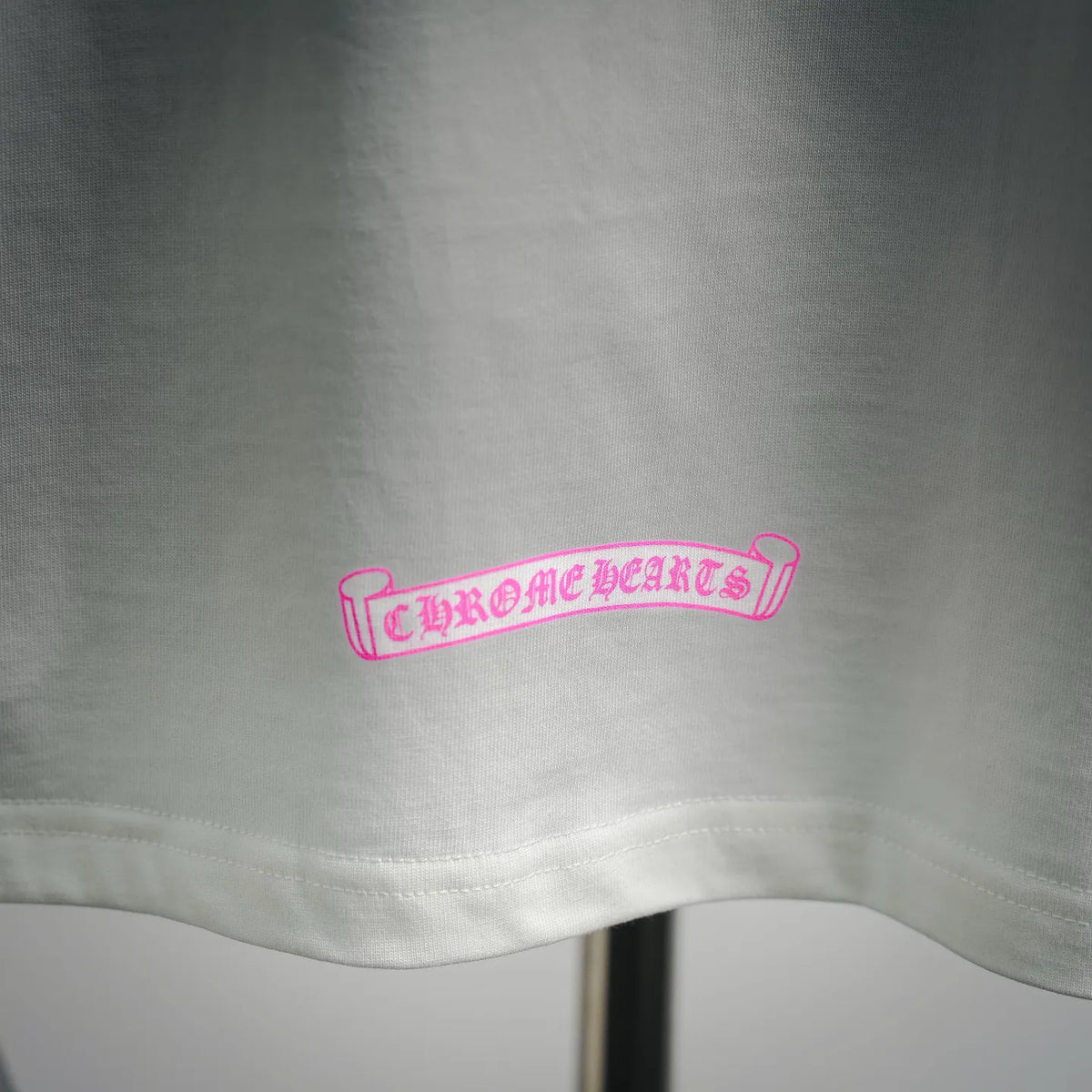 White T-shirt hem with small pink banner graphic near the bottom