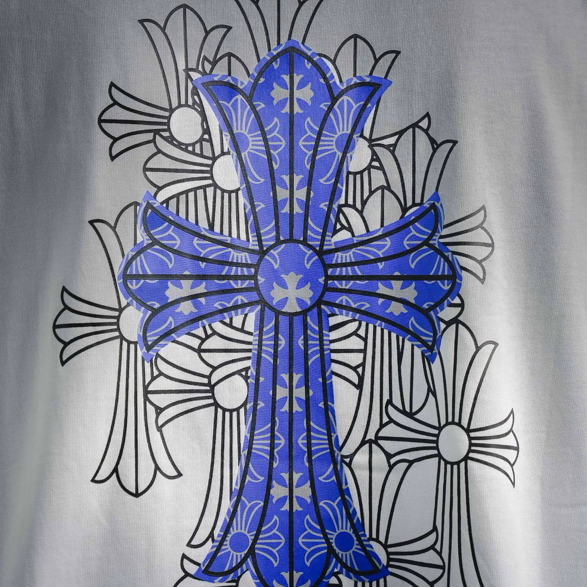 Close-up of blue cross print with decorative floral line art on white T-shirt