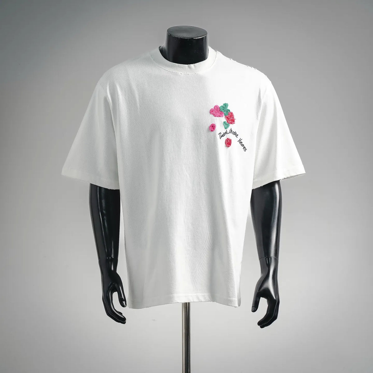 White short-sleeve graphic T-shirt with small colorful floral patches and cursive text